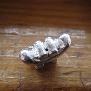 May include: A silver charm in the shape of a banana with a small hole in the center.