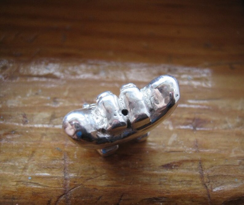 May include: A silver charm in the shape of a banana with a small hole in the center.