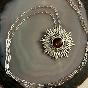 K&ouml;nnte beinhalten: Eine silberne Halskette mit einem Sonnenanh&auml;nger, der mit einem braunen Edelstein verziert ist. Die Kette ist in einem zarten, verlinkten Stil.