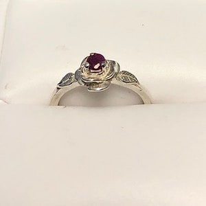 May include: A silver ring with a rose design and a small red gemstone in the center.