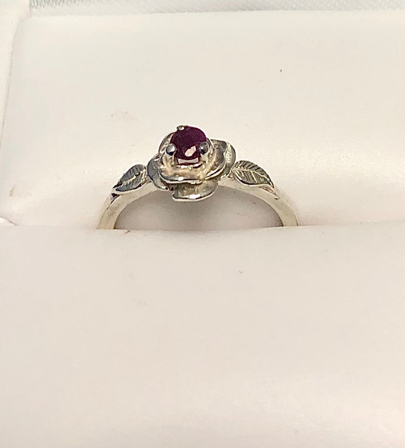 May include: A silver ring with a rose design and a small red gemstone in the center.