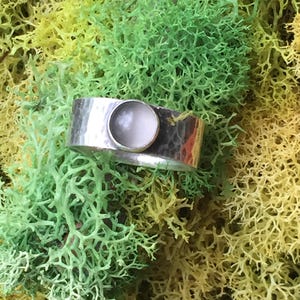 Puede incluir: Un anillo de plata con acabado martillado y una piedra blanca engastada en el centro.