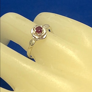 May include: A silver ring with a red gemstone set in a rose design.