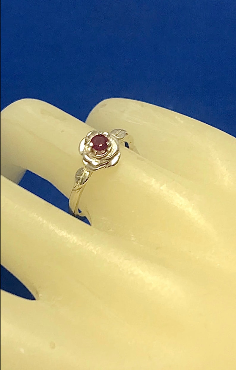 May include: A silver ring with a red gemstone set in a rose design.