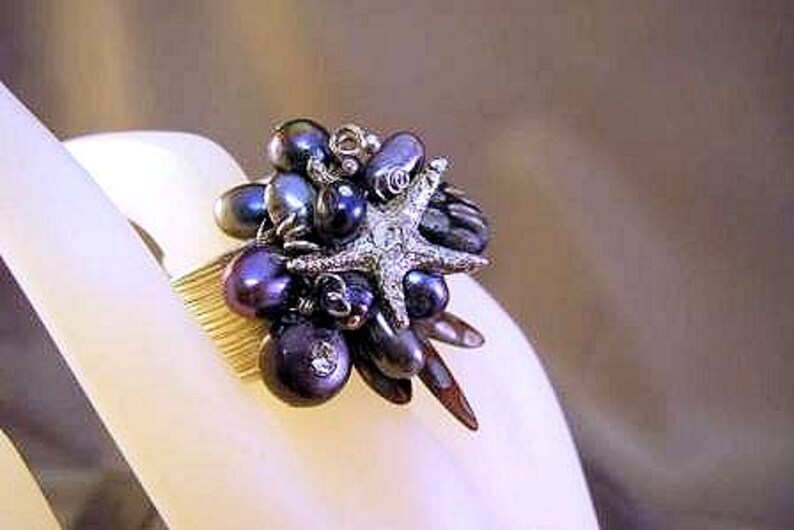 May include: A gold ring with a cluster of dark purple and black pearls, a silver starfish, and other decorative elements.