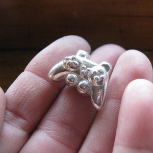May include: A silver-colored pendant shaped like a video game controller. The pendant has a detailed design with buttons and a joystick.