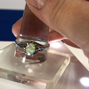 Puede incluir: Un anillo de plata con una piedra de &oacute;palo ovalada. El &oacute;palo presenta un arco&iacute;ris de colores, incluyendo verde, azul y morado.