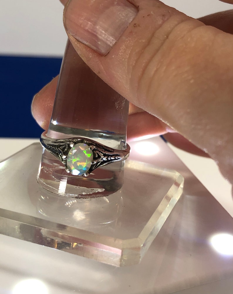 Puede incluir: Un anillo de plata con una piedra de &oacute;palo ovalada. El &oacute;palo presenta un arco&iacute;ris de colores, incluyendo verde, azul y morado.