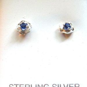 Op de afbeelding: Een paar oorbellen van sterling zilver met een blauwe edelsteen in een getextureerd bloemmotief.