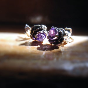 May include: A pair of silver earrings with purple gemstones set in a floral design.