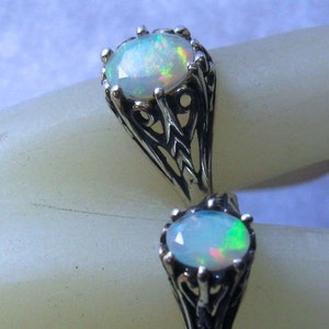 Puede incluir: Un anillo de plata con dos piedras de &oacute;palo engastadas en intrincados dise&ntilde;os de filigrana. Los &oacute;palos son iridiscentes con destellos de verde, azul y rosa.