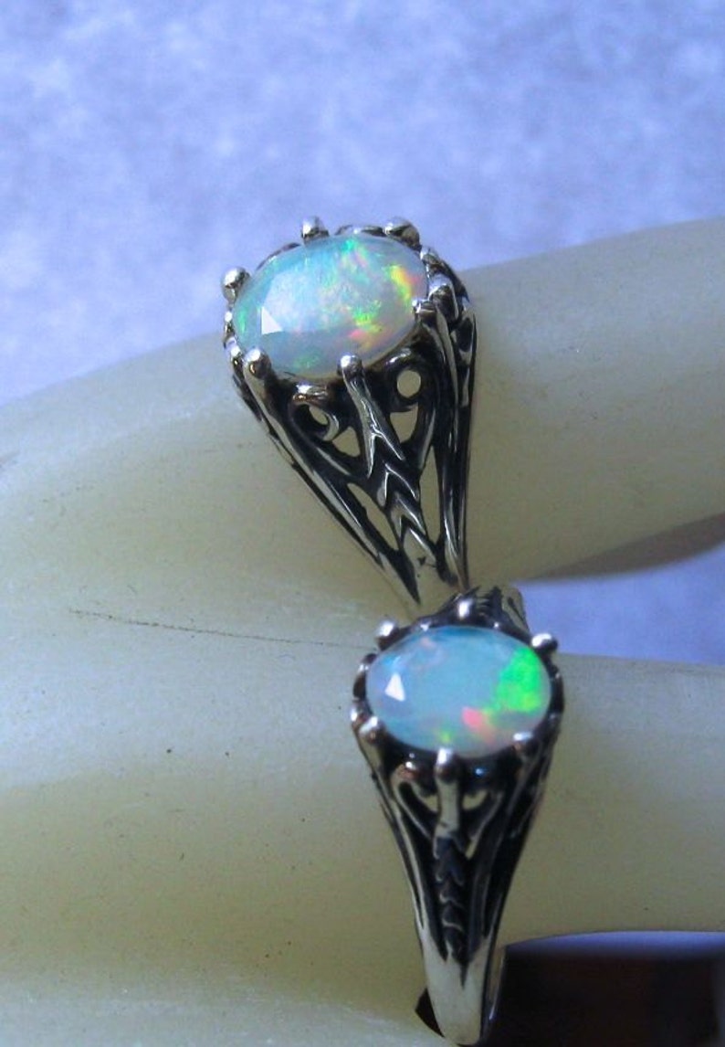 Puede incluir: Un anillo de plata con dos piedras de &oacute;palo engastadas en intrincados dise&ntilde;os de filigrana. Los &oacute;palos son iridiscentes con destellos de verde, azul y rosa.