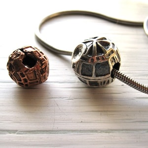 May include: Two silver and copper metal beads with intricate designs. The silver bead is on a silver chain. The copper bead is a separate piece.