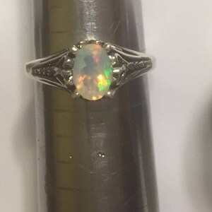 Puede incluir: Un anillo de plata con una piedra de &oacute;palo de forma ovalada. El &oacute;palo tiene una base blanca con destellos de verde y naranja.