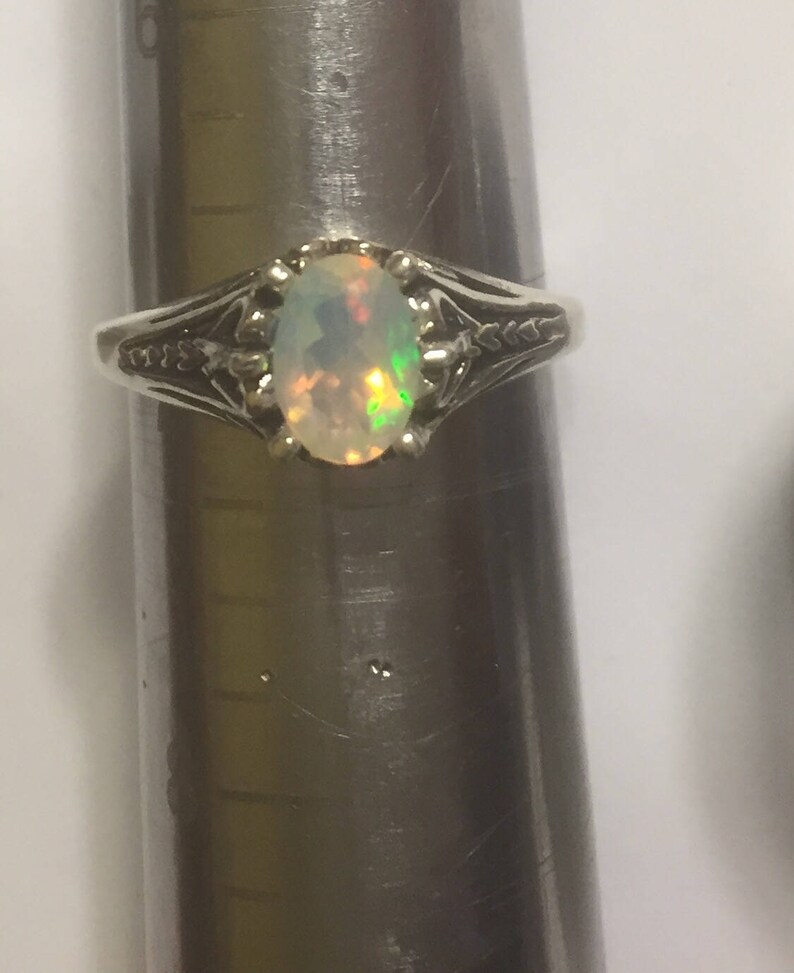 Puede incluir: Un anillo de plata con una piedra de &oacute;palo de forma ovalada. El &oacute;palo tiene una base blanca con destellos de verde y naranja.