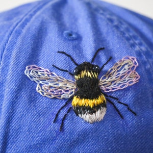 Handstitched bumble bee on a corn flower blue baseball cap. Featuring beaded eyes and delicately stitched wings.