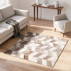 Puede incluir: Alfombra rectangular con un patrón geométrico en blanco, marrón y gris. La alfombra presenta un diseño de cubos 3D repetido. Se coloca sobre un suelo de madera en un salón, cerca de un sofá y un sillón.