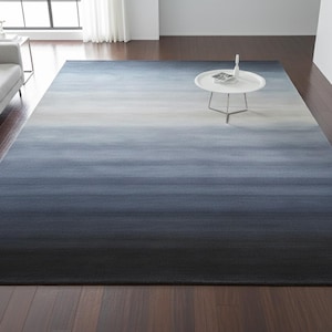 Pode incluir: Um grande tapete retangular com um design gradiente. O tapete transita de cinza claro no topo para azul marinho escuro na parte inferior. O tapete é colocado em um piso de madeira escura.