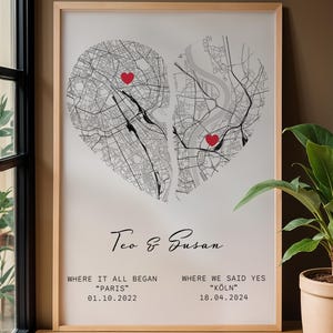 Peut inclure: Impression encadrée avec un design en forme de cœur divisé en deux cartes de villes, chacune avec un cœur rouge. Les noms "Teo & Susan" sont écrits en cursive. Le texte en dessous indique "WHERE IT ALL BEGAN PARIS 01.10.2022" et "WHERE WE SAID YES KOLN 18.04.2024".