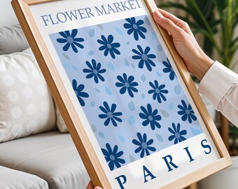 May include: A framed art print featuring a light blue background with a pattern of dark blue flowers and raindrops. The text "FLOWER MARKET PARIS" is displayed in a clean, sans-serif font. The frame is made of light-colored wood.