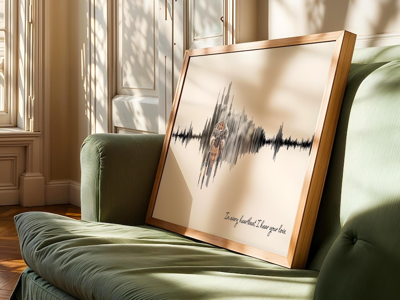 Puede incluir: Una obra de arte enmarcada con un marco de madera clara, que presenta un dise&ntilde;o de onda de sonido con una ilustraci&oacute;n de pareja. La obra de arte se muestra en un sof&aacute; verde. El texto en la parte inferior dice: "In every heartbeat I hear your love."