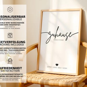 May include: A framed print with the word "zuhause" in a stylish script, with coordinates and names below. The print is in a light wood frame and is displayed on a wooden chair. The image also includes text in German and English.