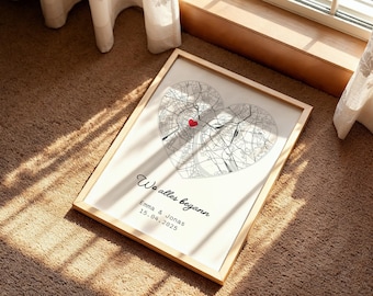 Op de afbeelding: Ingelijste print met een hartvormig kaartontwerp en een rood hart dat een locatie markeert. De tekst "We alles begann" staat boven de namen Emma & Jonas en de datum 15.04.2025. De lijst is van licht hout.