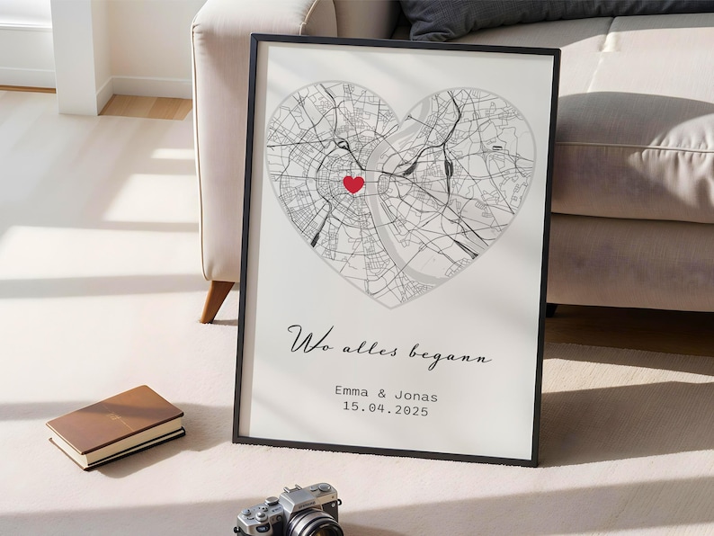May include: Framed print featuring a heart-shaped map with a red marker. The map is detailed with city streets and a central point. Below the map, the text reads "Wo alles begann", with names and a date.