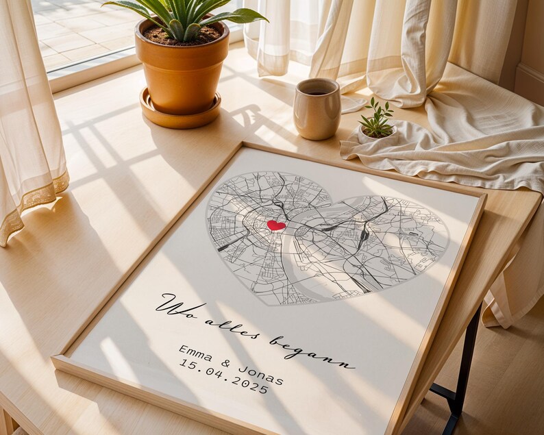 May include: A framed map print featuring two overlapping heart-shaped city maps in black and white, with a red heart marking a location. The print includes the text "Wo alles begann" and names and a date.