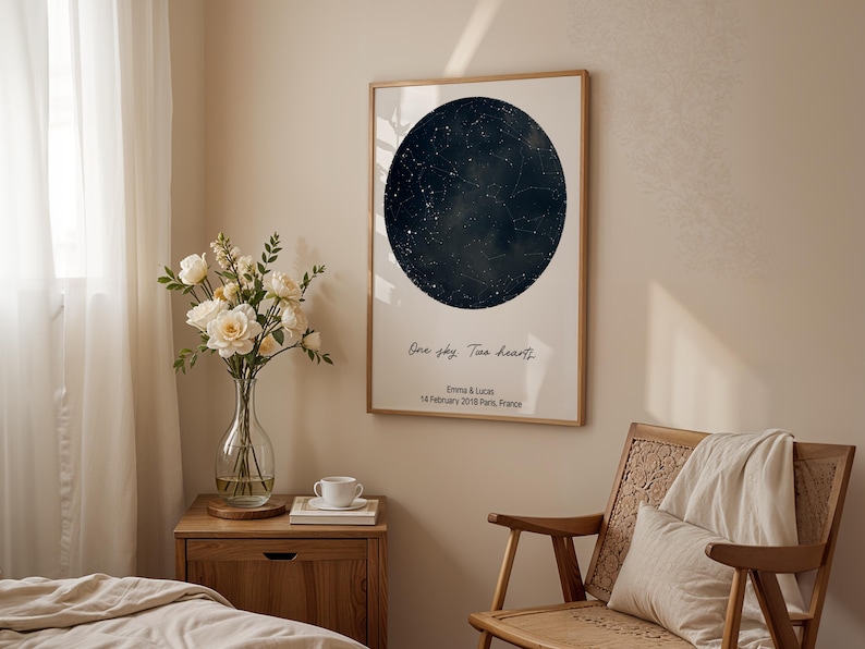 Peut inclure: Impression encadr&eacute;e repr&eacute;sentant une carte c&eacute;leste bleu fonc&eacute; dans un design circulaire. L'impression comprend le texte "One sky. Two hearts." et les noms "Emma & Lucas" avec une date et un lieu. L'impression est affich&eacute;e dans une pi&egrave;ce avec une chaise en bois et un vase de fleurs.