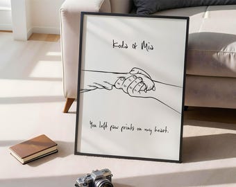 May include: Black framed art print with a minimalist line drawing of two hands holding a paw. The text "Koda & Mia" is above the drawing, and "You left paw prints on my heart" is below. A book and camera are in the foreground.