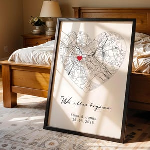 May include: Framed print featuring a heart-shaped map with a red heart marking a location. The print includes the text "Wo alles begann" and the names "Emma & Jonas" with a date. The frame is black.