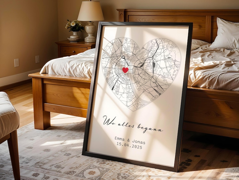 May include: Framed print featuring a heart-shaped map with a red heart marking a location. The print includes the text "Wo alles begann" and the names "Emma & Jonas" with a date. The frame is black.