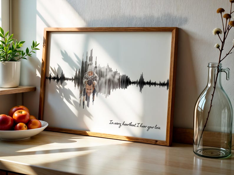 Puede incluir: Una impresi&oacute;n enmarcada con un marco de madera muestra un dise&ntilde;o de onda de sonido en blanco y negro con una superposici&oacute;n de fotos. El texto "In every heartbeat I hear your love" est&aacute; escrito en cursiva. La impresi&oacute;n est&aacute; sobre una superficie de madera.