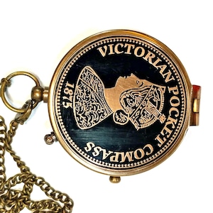 Puede incluir: Brújula de bolsillo victoriana de latón antiguo con cadena. La brújula presenta una esfera negra con el perfil dorado de una mujer y las palabras "Victorian Pocket Compass 1875".