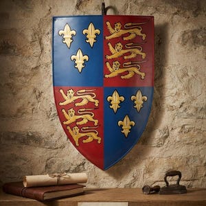 May include: A shield featuring a quartered coat of arms with gold fleurs-de-lis on blue and gold lions on red. A label below reads: Historical Coat of Arms Shield - 14th C. Replica. The shield is mounted on a wall above a wooden shelf with a book.