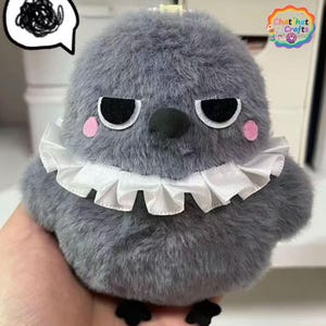 Puede incluir: Un pájaro de peluche gris con un cuello blanco con volantes, ojos negros y mejillas rosadas. El pájaro tiene una expresión gruñona y pequeños pies negros. La imagen incluye un bocadillo con garabatos y un logo que dice "Chat' hat Crafts".