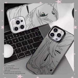May include: Clear phone cases with a black and white anime-style illustration of a character's face. The cases have a camera lens protector that says "SO COOL". The cases are on a laptop keyboard. Text on the case reads "BEST CHOICE FOR YOUR".