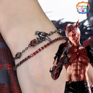 Może przedstawiać: Dwurzędowa bransoletka z ciemnym metalowym łańcuszkiem z motywem ptaka i róży oraz pasmem czerwonych dżetów. Bransoletka jest noszona na nadgarstku. Obraz zawiera również postać z rogami i krukiem.