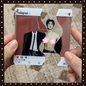 Puede incluir: Un llavero acrílico transparente con forma de publicación de Instagram, con una foto de un hombre con traje y otro sin camisa. El llavero está dividido en dos partes, con el logotipo y el texto de Instagram en la parte superior.