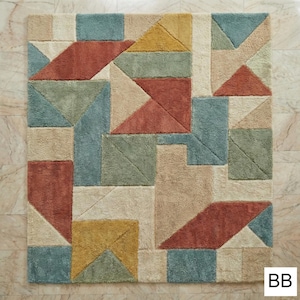 May include: Geometric patterned area rug in shades of beige, blue, green, yellow, and rust. The rug features a repeating pattern of triangles and rectangles. The rug is square and has a soft, plush texture.