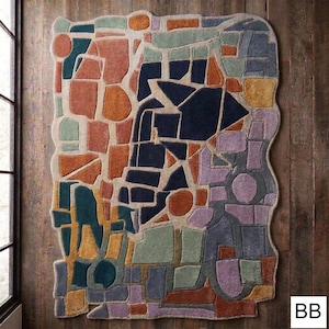 May include: A colorful area rug with an abstract design. The rug features a patchwork of geometric shapes in shades of orange, blue, green, purple, and beige. The rug is rectangular with a wavy border and is placed on a wooden floor.
