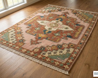 May include: A rectangular area rug featuring a central cream-colored medallion on a rust-orange field, surrounded by a light pink border with geometric floral motifs in teal, yellow, and brown. The rug has short white fringe on both ends.