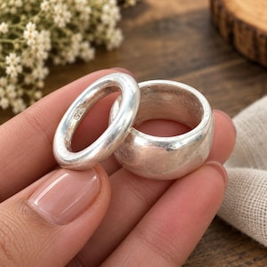 May include: Two silver rings with a smooth, polished finish. One ring is a thin, rounded band, while the other is a wider, thicker band. The interior of the thinner ring is clearly stamped with the hallmark S925, indicating sterling silver composition.