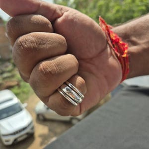 May include: A set of three stacked silver rings with a smooth, polished finish. The rings are worn together on a finger, featuring a simple, rounded band design that creates a layered appearance. The metal has a bright, reflective surface.