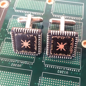 Puede incluir: Un par de gemelos con fondo negro y un diseño de estrella dorada. Los gemelos tienen forma de chips de computadora con un borde texturizado.