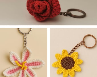 Könnte beinhalten: Eine Sammlung handgefertigter gehäkelter Schlüsselanhänger mit floralen Designs. Die Schlüsselanhänger umfassen eine rote Rose, eine weiß-rosa Lilie und eine gelbe Sonnenblume. Jeder Schlüsselanhänger hat einen Metallring und eine Kette.