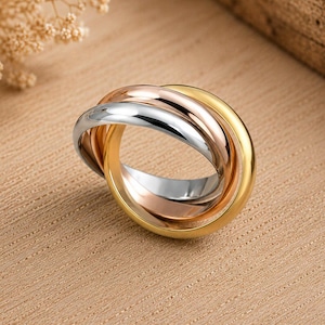 May include: A tri-colour rolling ring featuring three interlocking bands in polished yellow gold, rose gold, and silver-toned metal. The smooth, rounded bands are intertwined to form a single cohesive piece of jewellery with a reflective finish.