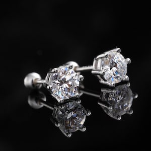 Puede incluir: Un par de pendientes de plata con grandes gemas redondas y transparentes. Los pendientes están engastados en un engaste de garras, que refleja la luz. El fondo es negro.