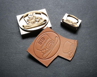 May include: A leather craft image featuring a metal stamp and a stamped leather piece. The stamp has a cowboy hat design with the text "BTD LEATHERWORKS". The leather piece is brown and shows the hat design.